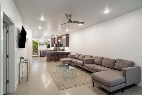 Spacious open-concept living area with plush sectionals, a Smart TV, and modern ceiling fan, seamlessly flowing into the kitchen.