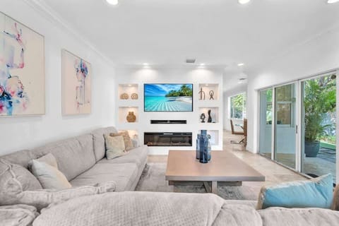 Relax in this bright, stylish living room featuring a plush sectional, large TV, and modern décor. Enjoy a movie, read a book, or soak in the seamless indoor-outdoor flow—perfect for unwinding.