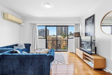 Relax in a bright living room with a plush blue sofa, city views from the window, and a sleek entertainment center.