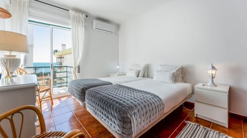 Relax in a serene coastal bedroom with twin beds, air conditioning, and balcony access overlooking the ocean. #OceanRetreat #CoastalCalm #SeaBreezeSleep