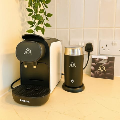 A chic coffee corner featuring a sleek black and white Philips coffee machine, a L’OR milk frother, and supply of coffee pods. Ideal for your morning brew, it perfectly complements this cozy, well-lit kitchen.