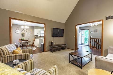 Spacious living room with vaulted ceilings and hardwood carpeted floors. Features comfortable seating, a TV, and an open-concept dining area. Perfect for relaxing and entertaining.