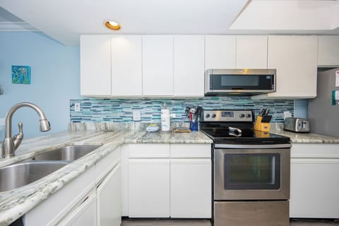 This kitchen features a spacious design, a beautiful granite countertop, and a stylish blue mosaic backsplash