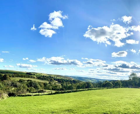 Green field overlooking rolling hills under a blue sky with scattered clouds