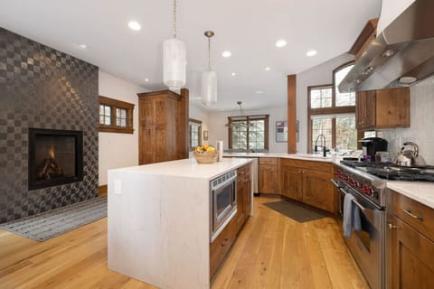 Warm, modern kitchen with wood cabinetry, white countertops, and a fireplace.