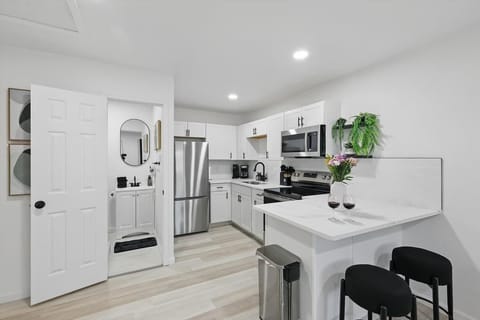 “Bright Kitchen in Unit 2 with Modern Touches” This fully equipped kitchen features stainless steel appliances, stylish finishes, and a cozy breakfast bar with 2 stools — plus a peek into the clean, modern bathroom.