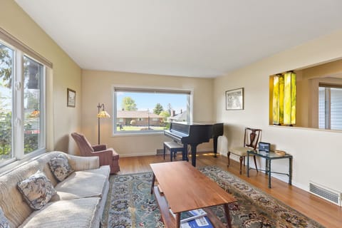 Elegant living room w/ comfy chairs, large windows, and a baby grand piano