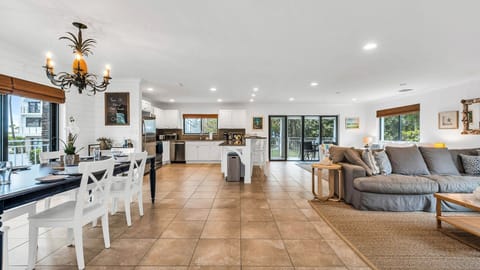 Bright and coastal dining area with a table set for eight, offering views of the charming homes and condos along the street. Features include dinner service for eight, a bar cart ready for cocktail hour, and access to the kitchen for seamless entertainment