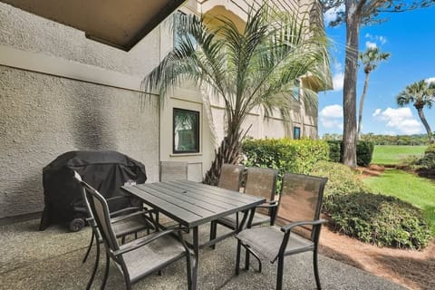 A ground-level outdoor dining area with a metal table and four chairs, surrounded by lush landscaping and palm trees.