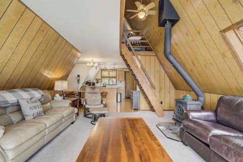 The heart of the cabin—this open-concept space ties together the cozy living area, full kitchen, and loft access with warm wood accents and a classic wood-burning stove for mountain ambiance.