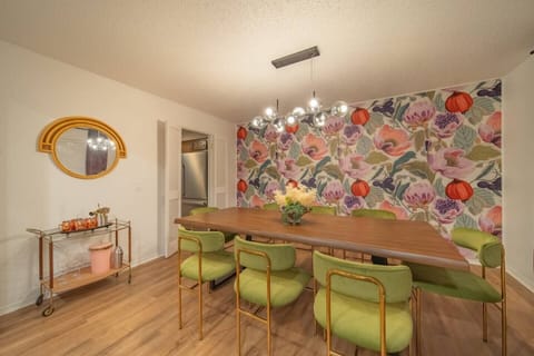 This vibrant dining room features a bold floral accent wall, modern lighting, and stylish seating—perfect for gathering and entertaining in a lively setting.