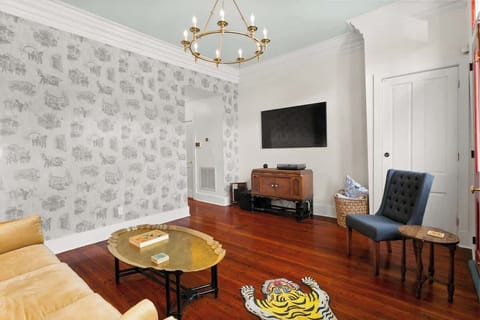 Charming living room with custom wallpaper, elegant molding, and rich wood floors. Relax on the velvet sofa with a smart TV and playful décor, perfect between French Quarter adventures.