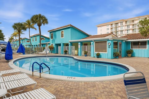 A turquoise pool area is surrounded by palm trees and colorful buildings at Sand Dune Shores in Palm Beach Shores, Florida.