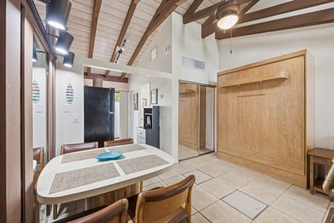 A small dining area with a round table and wood chairs sits beneath exposed beam ceilings in the studio.