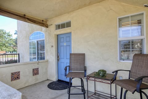 The exterior features a small covered patio with textured beige stucco walls, a bright blue entrance door, and a high-top bistro set.