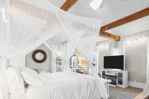 Spacious primary bedroom with exposed beams, a canopy bed, and a glowing window cupola overhead
