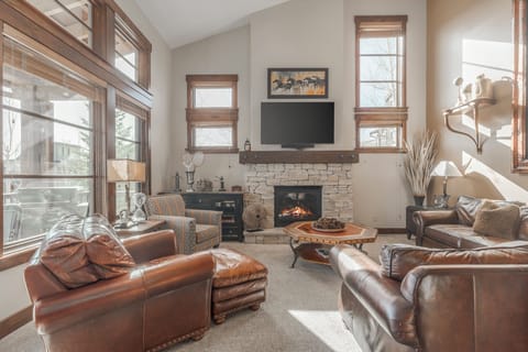 Cozy, sun-filled living room with vaulted ceilings, rustic charm, and a stone fireplace centerpiece.