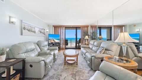 This spacious living room features plush reclining sofas, a large flat-screen TV, and stunning beach views.