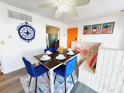 This charming dining area offers a cozy built-in bench and stylish blue chairs around a dark wood table, perfect for enjoying meals together. The bright space is enhanced by colorful artwork and a unique wall clock, creating an inviting atmosphere for family and guests.