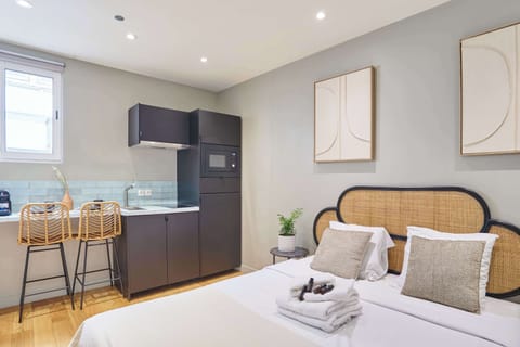 Studio avec lit double, TV, coin repas et cuisine ouverte équipée.