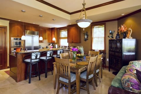 Open concept dining and kitchen area with seating for six, tropical art, and pendant lighting.