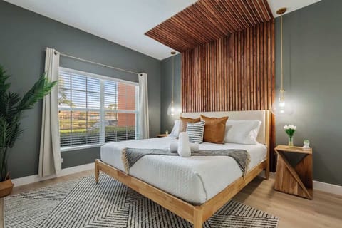 Modern bedroom with a sleek wood accent wall. Features a cozy bed with stylish pillows, pendant lighting, and natural decor. Enjoy ample natural light through large windows. Perfect for a relaxing stay. Book your serene getaway today!