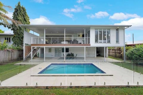 The back of the home showcases a sparkling pool, a lush fenced yard, and expansive upper and lower outdoor living areas designed for relaxation and entertaining.