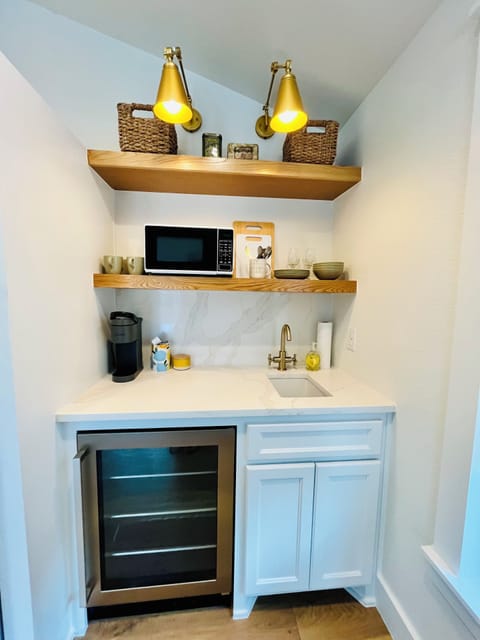 Kitchenette with refrigerator, microwave, coffee machine, small sink.