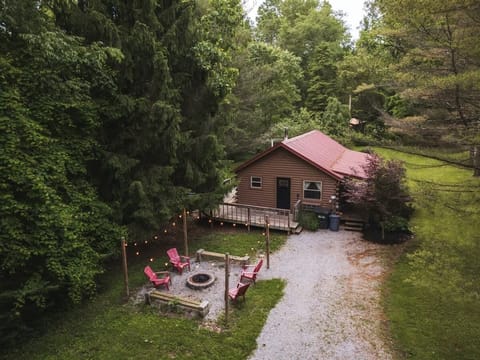 Charming forest cabin with a cozy fire pit surrounded by red chairs, perfect for evening gatherings. A serene natural retreat with lush greenery and warm outdoor lights to set the mood ✨