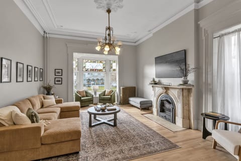 Living room complete with 12 foot tall ceilings, exuding 20th century character with a marble fireplace, original chandelier, crown molding, intricate wood trim, and stained glass windows
