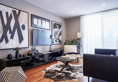 Unwind in the art-filled living area where a Chesterfield, a 70-inch smart TV, built-in subwoofer, and curated design books invite you to relax in style.