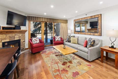 Cozy living area featuring a plush sectional sofa, stone fireplace with mounted TV, and a sliding door that opens to a private patio.