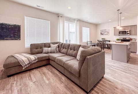 Spacious open-concept living area with cozy sectional, bright windows, and seamless kitchen connection.
