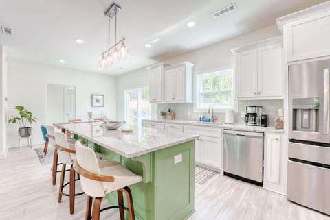 Bright and inviting modern kitchen featuring a large green island with seating, white cabinetry, stainless steel appliances, and ample natural light.