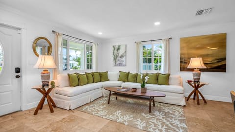 This bright and airy living room offers plenty of space for up to 6 guests to relax in comfort. Featuring a wraparound sectional with plush green accent pillows, a smart TV, and tasteful tropical decor, it's the perfect place to unwind after exploring WPB