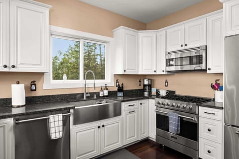 Cook with a view in this fully equipped kitchen featuring stainless steel appliances, granite countertops, and sweeping lake and forest scenery.