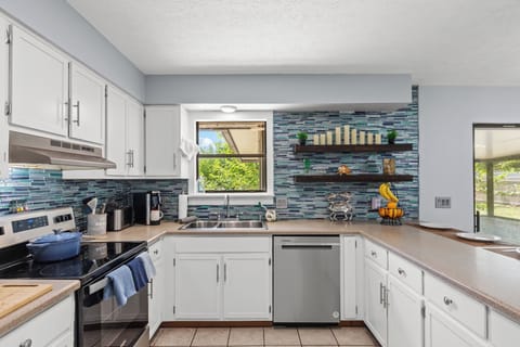 Stylish and fully stocked kitchen featuring modern appliances, open shelving, and a bright window overlooking the backyard. With ample counter space and all the essentials, it's perfect for everything from morning coffee to home-cooked meals.