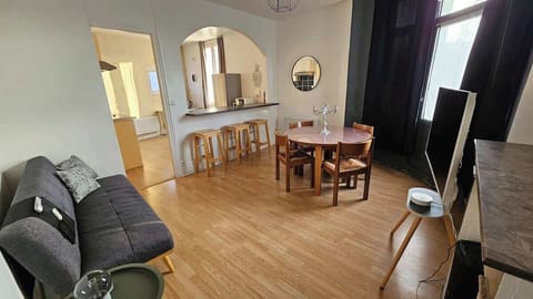 Salon semi ouvert sur la cuisine, avec canapé convertible pour une personne, télévision et espace repas.