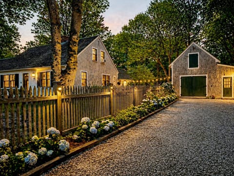 Front of home with fully fenced-in yard and a driveway lined with hydrangeas.