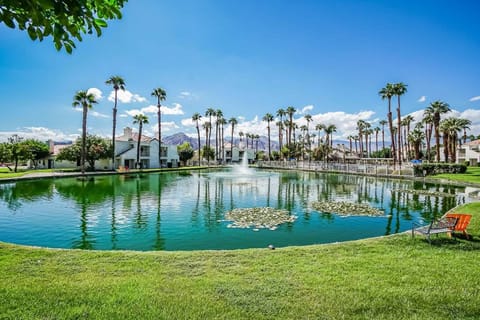 Palm trees surround a tranquil pond with a fountain and mountain backdrop