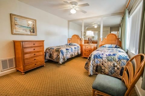 This cozy bedroom features two twin beds with colorful bedding, a wooden dresser, and ample natural light.