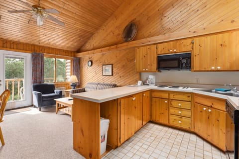 The open kitchen layout seamlessly flows into the living area, where wooden accents and a comfortable seating arrangement create an inviting atmosphere.