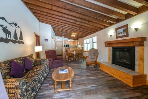 Inside the Timbers at Island Park condo, the open living space boasts a warm wood-burning fireplace, a full kitchen, and a comfortable lounge area, perfect for relaxing after a day of exploration.