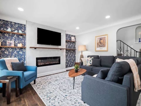 Unwind in this stylish living room featuring a cozy sectional, electric fireplace , and smart TV . Floral accents, modern décor, and soft lighting make it the perfect space to relax after a day out. ️