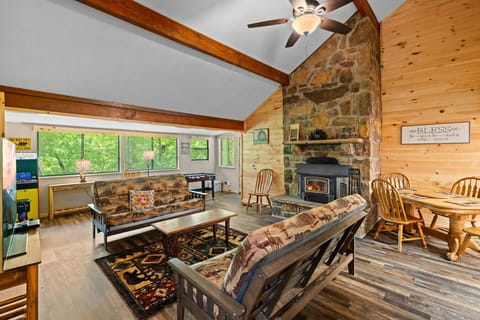 Gather around the crackling wood stove in this cozy living space, where tall ceilings, warm wood walls, and woodland decor invite you to truly unwind.
