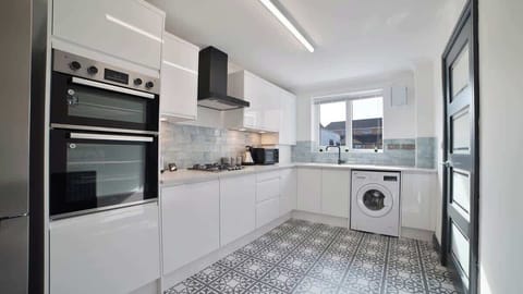 Sleek and modern full kitchen featuring glossy white cabinets, built-in double ovens, a gas cooktop, washing machine, and patterned tile flooring—designed for both style and functionality.
