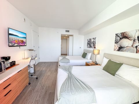 Spacious bedroom with a two beds, flat-screen TV, and bright natural lighting.