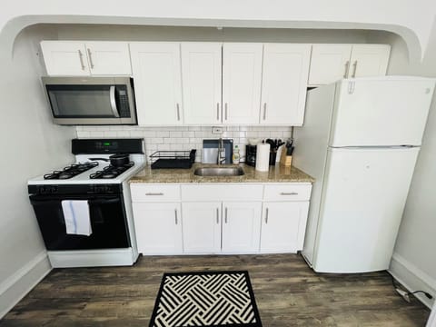 Bright and updated kitchen featuring white cabinets, modern backsplash, full-size fridge, microwave, and gas stove. Includes open shelving, ample counter space, and contemporary flooring—ideal for everyday cooking and casual dining.