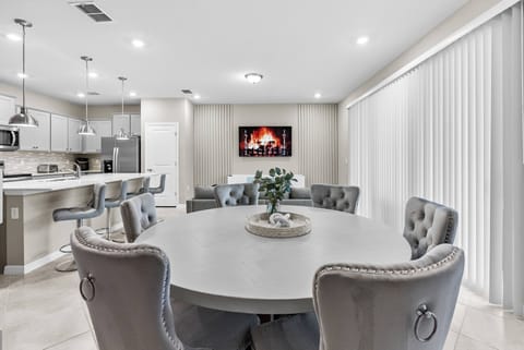 Come together at the stylish round dining table with plush gray chairs, perfect for sharing meals. Large windows fill the room with natural light, and a cozy electric fireplace creates a warm, inviting ambiance for everyone.