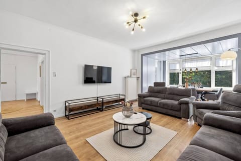 Das moderne Wohnzimmer mit komfortablen Sofas und großem Fernseher lädt zum Entspannen ein und geht nahtlos in den lichtdurchfluteten Essbereich über.